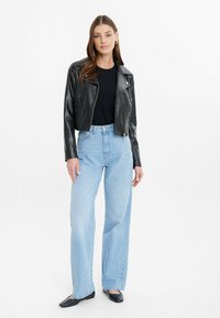 Giacca di pelle nera corta sopra un top nero, abbinata a jeans a gamba larga a vita alta di colore blu chiaro e scarpe nere basse. Design e texture pulite.