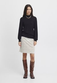 Černý pulovr s dlouhým rukávem, krémová sukně s černými puntíky, hnědé kozačky po kolena a zlatý řetízek. Jednoduchý, moderní outfit.