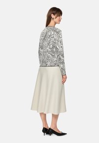 Black and white illustrated jacket; soft fabric; cream A-line skirt; leather pointed-toe heels; minimalistic silver earrings; back view.