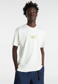 Camiseta de algodón crema de mangas cortas, con un colorido logo gráfico "Vans Off the Wall" en la parte delantera. Diseño clásico de cuello redondo.