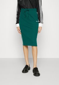 Sievstenliivi hame, jossa on istuva siluetti, joustava vyötärönauha ja nyöri. Mukana valkoiset sivuraidat ja Adidas-logo edessä.