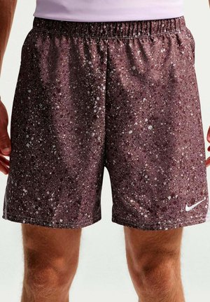 Weinrote Sportshorts mit weißem gesprenkeltem Muster und weißem Nike Swoosh-Logo, getragen von einer Person, die mit entspannt herabhängenden Armen steht.