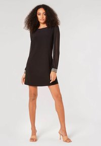 Schwarzes Kleid mit langen durchsichtigen Ärmeln, quadratischem Ausschnitt und verzierten Manschetten. Glatter Stoff mit einer taillierten Silhouette, die bis zur Mitte des Oberschenkels reicht.