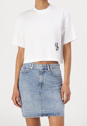 Witte, kortgeknipte katoenen T-shirt met een zwart logo aan de linkerkant, gecombineerd met een lichtblauwe high-waisted spijkerrok met een geruit patroon.