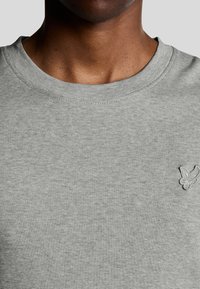 Grå bomulds sweatshirt med rund hals og en glat tekstur samt et lille broderet logo på venstre bryst. Enkel design og klassisk pasform.
