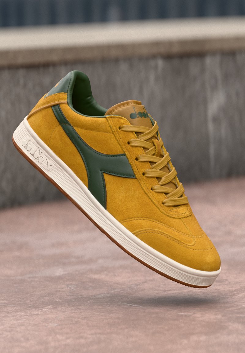 Baskets en daim jaune moutarde avec des accents verts, dotées d'un bout rond, de lacets plats et d'une semelle en caoutchouc avec un motif texturé.