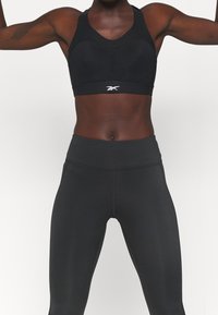 Black sports bra with mesh ventilation details, paired with high-waisted black leggings in a smooth, stretchy fabric. Simple, functional design.