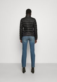 Czarna pikowana kurtka puchowa z wysokim kołnierzem, w połączeniu z jasnoniebieskimi prostymi dżinsami i czarnymi botkami na obcasie, widok z tyłu.