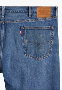 Jeans de denim azul con un parche de marca de cuero, costuras naranjas y un diseño de bolsillo trasero curvado que presenta una etiqueta de logo roja.