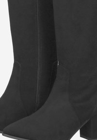 Bottines en daim noir avec un bout pointu, un petit talon bloc et un détail de fermeture éclair sur le côté. Texture lisse sans motifs ni accents visibles.