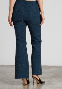 Pantalones de campana en color marino con un patrón de encaje texturizado, adornados con un ligero brillo, combinados con zapatos de tacón negro brillantes.