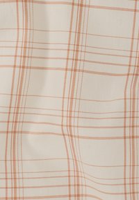 Tissu en coton avec un fond crème et un motif à carreaux orange subtil. Texture lisse avec des lignes croisées formant un motif en grille.