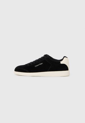 Black suede sneaker with white rubber sole. Features rounded toe, lace-up design, and logo detail on the side.
