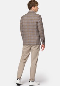 Brązowa marynarka w kratę z jasnoniebieskimi akcentami, zestawiona z beżowymi spodniami i białymi trampkami, widok od tyłu. Dopasowany krój, gładka faktura.