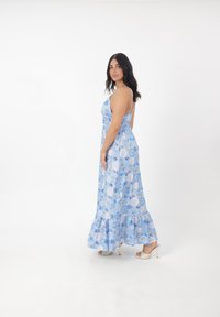 Blå blommig maxikjol med tunna band, volangsläpp och åtsittande bodice. Har ett lätt, flödande tyg med mönster av blå och vita rosor.