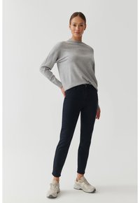 Sivi dugi rukav pleteni pulover kombiniran s tamnoplavim uskim trapericama i svijetlosivim sportskim cipelama. Outfit ima ležeran, moderan izgled.