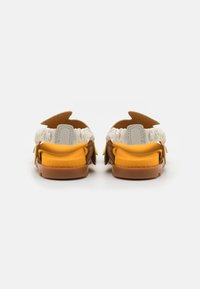 Ruskeat ja keltaiset sandaalit valkoisella joustovyöllä, pyöreällä kärjellä ja ainutlaatuisella leikkuumuotoilulla takana. Varustettu tekstuuripohjalla.