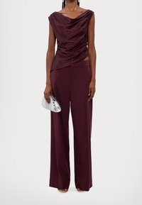 Haut drapé bourgogne avec un large décolleté associé à un pantalon large assorti. Accessoirisé avec une pochette argent métallique. Texture lisse.