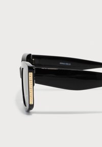 Black rectangular sunglasses with thick frames. Features a gold-toned logo detail on the temples. Smooth, glossy finish throughout.