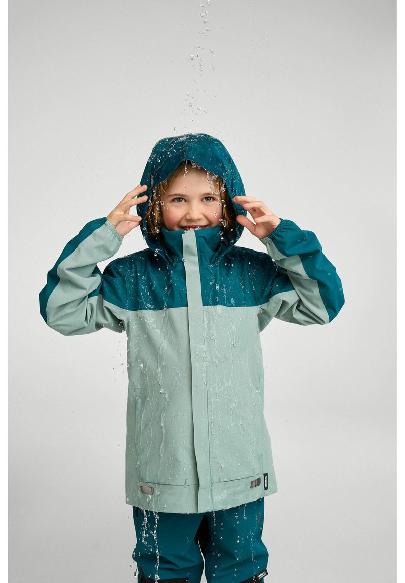 Veste imperméable bleu sarcelle et vert clair avec capuche, dotée d'une fermeture éclair à l'avant, de manches longues, et de gouttelettes d'eau s'écoulant sur le tissu.