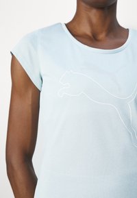 Vaaleansininen lyhythihainen paita pehmeästä kankaasta, jossa edessä valkoinen hyppivää pumaa kuvaava ääriviiva. Pyöreä pääntie.