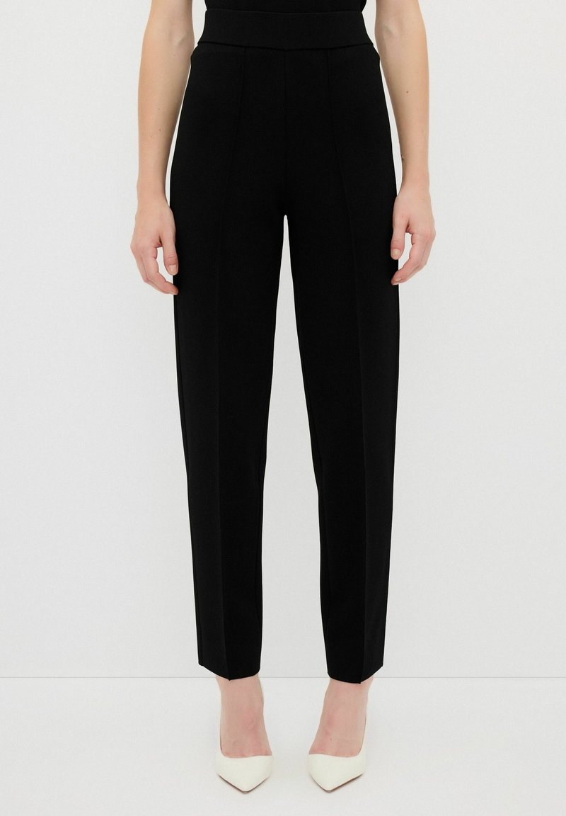 Pantalons noirs ajustés avec une taille haute, jambes légèrement fuselées et détails de couture à l'avant. Tissu lisse sans motifs visibles ni poches.