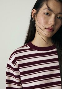 Sweter dziany z bordowymi i kremowymi poziomymi paskami, okrągłym dekoltem, miękką teksturą i widocznym detalem żebrowanego kołnierza.