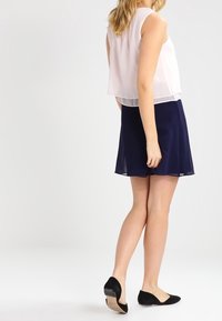 Bez rukávů, průhledný růžový top vrstvený přes tmavě modrou sukni. Černé baleríny s hladkým povrchem a nízkým podpatkem. Jednoduchý, elegantní design.