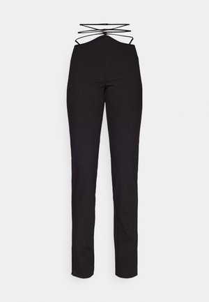 Pantaloni neri aderenti con un design a vita alta, caratterizzati da un dettaglio incrociato sul retro e una texture liscia. Cerniera e spacco alle caviglie.