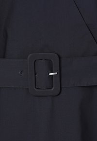 Gros plan d'une ceinture en tissu noire avec une boucle rectangulaire recouverte et un ardillon métallique qui maintient la ceinture à travers un trou.