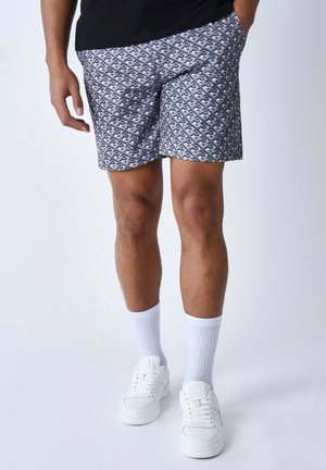 Bermudas con estampado en tonos de azul y blanco, que presentan un diseño geométrico, tejido ligero y un ajuste holgado. Llevadas con calcetines blancos y zapatillas.