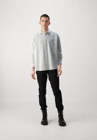 Lichtgrijze, gestreepte button-up shirt met lange mouwen, gecombineerd met zwarte broek en zwarte veterschoenen. Eenvoudig ontwerp, geen zichtbare patronen.