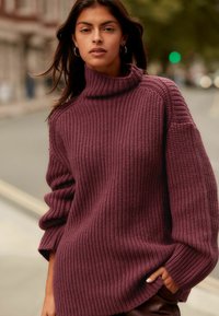 Dicker bordeauxfarbener Strickpullover mit einem hohen Kragen, weiten Ärmeln und einer gerippten Textur. Verfügt über einen entspannten Schnitt und seitliche Taschen.