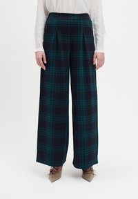 Weite Hosen aus navy- und grün-kariertem Stoff mit hohem Taillenbund und Falten. Das Material hat eine weiche Textur.