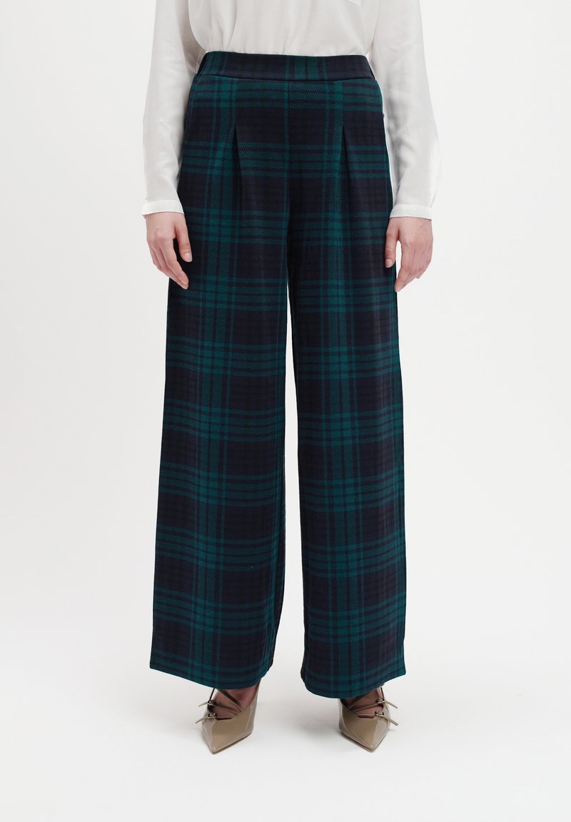 Weite Hosen aus navy- und grün-kariertem Stoff mit hohem Taillenbund und Falten. Das Material hat eine weiche Textur.