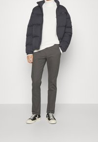 Czarna pikowana kurtka puchowa z poziomym wzorem przeszyć, biały golf, ciemnoszare spodnie oraz czarne sneakersy z białą podeszwą i detalami.