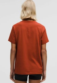 Rūsas krāsas īsām piedurknēm T-krekls, kas izgatavots no mīkstas auduma, ar taisnu piegriezumu, vienkāršu dizainu un nelielu aizmugures šuvju detaļu.