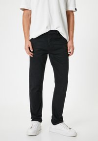 Vaqueros de mezclilla negros con corte recto, cinco bolsillos y cierre de botones. Combinados con una camiseta blanca holgada y zapatillas blancas.