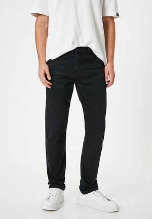 Vaqueros de mezclilla negros con corte recto, cinco bolsillos y cierre de botones. Combinados con una camiseta blanca holgada y zapatillas blancas.