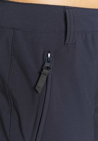 Zwarte broek van een gladde, rekbare stof. Heeft een ritszak met een matte zwarte trekker en een platte tailleband.