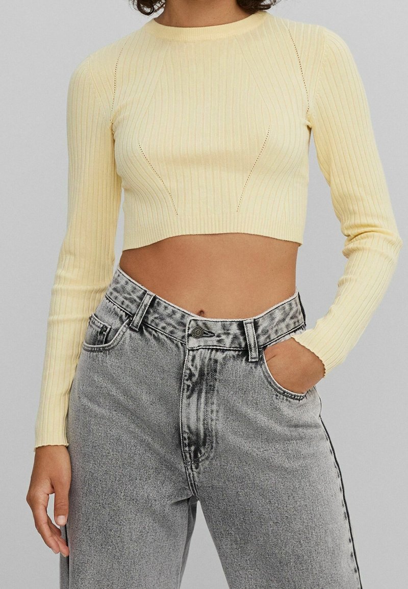 Top court jaune côtelé à manches longues, avec une coupe ajustée et des détails de couture subtils, associé à un jean gris taille haute.