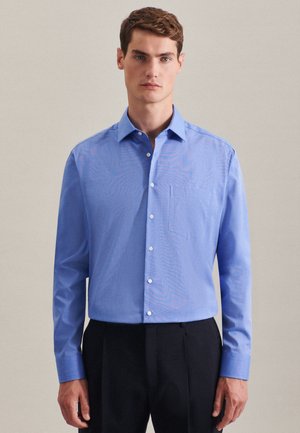 Camicia button-up azzurra con colletto a punta, taschino sulla sinistra del petto e maniche lunghe, abbinata a pantaloni scuri.
