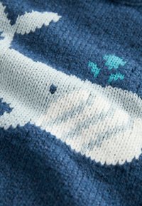 Close-up of blue knitted fabric featuring a white and light blue whale design with small teal water spouts.