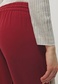 Red elastic waistband pants with a smooth texture, paired with a light gray ribbed long-sleeve top, featuring a rounded hem.