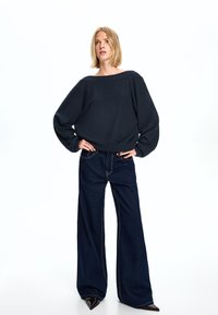 Marinblå kort sweatshirt med vid halsringning, tillsammans med högmidjade, vida mörk denimjeans med kontrasterande sömmar.