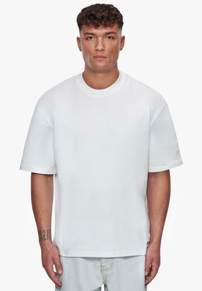 Hvid bomulds t-shirt med korte ærmer, afslappet pasform, rund halsudskæring og en diskret mærke-detail på venstre ærme. Glat tekstur.