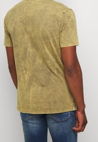 T-shirt à manches courtes vert olive en tissu doux avec une finition texturée, présentant un col arrondi et une coupe décontractée.