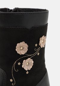 Czarna zamszowa sekcja butów z beżowymi, błyszczącymi aplikacjami w kwiaty połączonymi beżowymi przeszytymi winoroślami.
