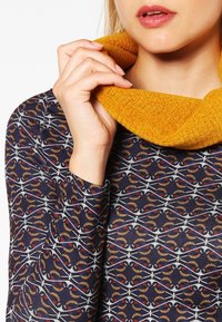 Maglia a maniche lunghe in blu navy con un intricato motivo multicolore; presenta un ampio colletto a imbuto giallo senape e tessuto a maglia testurizzato.