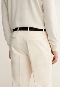 Pantalones de color claro con un diseño elegante, que cuentan con un cinturón negro. Bolsillos traseros con botones, textura suave y ajuste entallado.